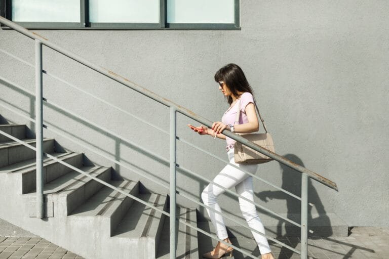 A worried young lady sitting on the stairs waits for a mobile network signal in city.